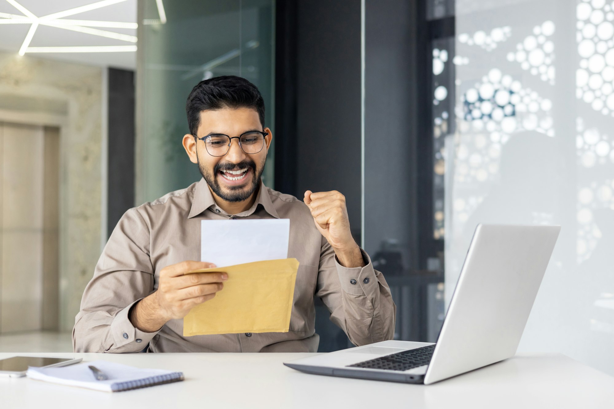 Excited businessman reading good news letter at the office desk